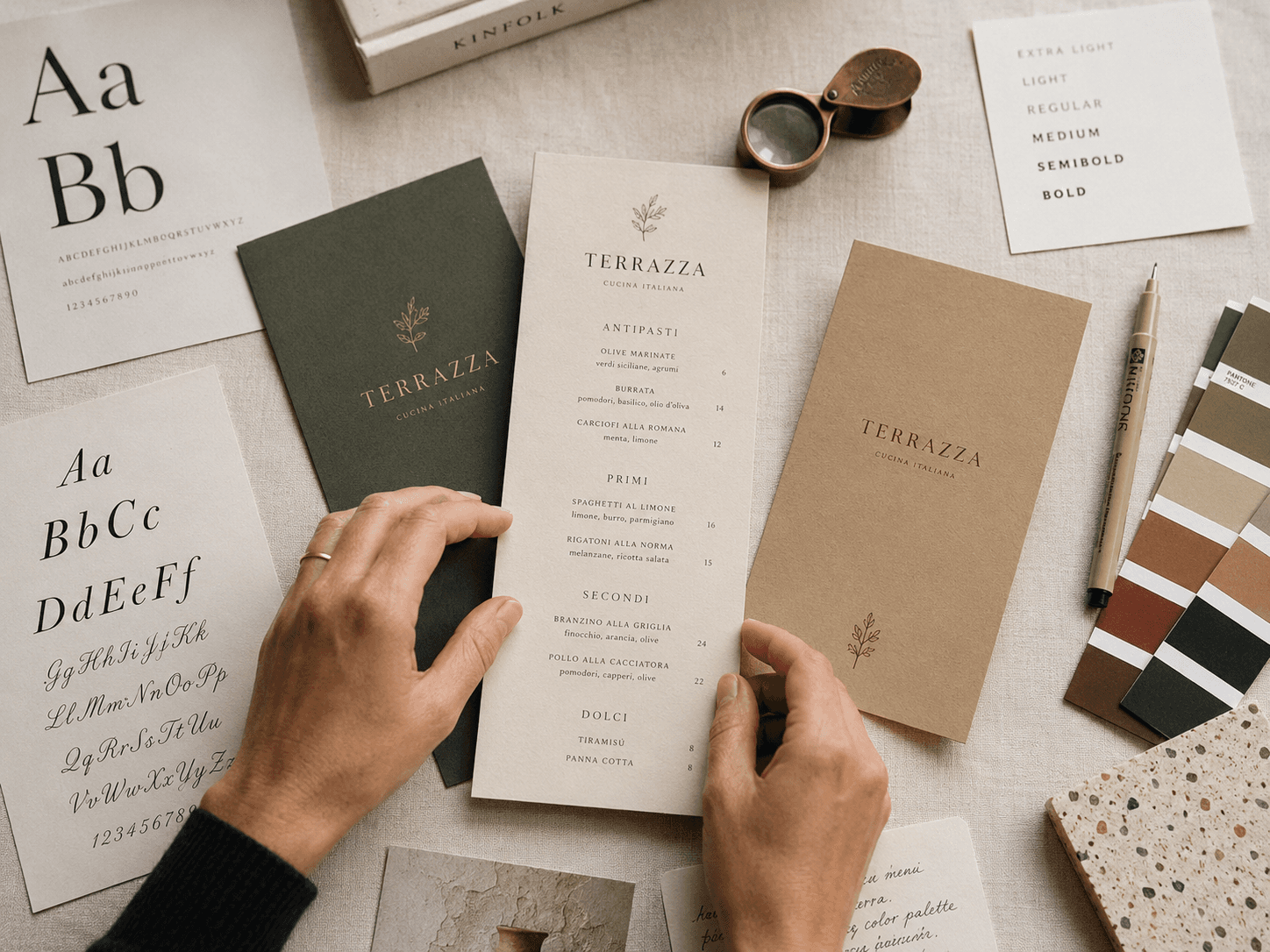 Hands holding a Terrazza menu surrounded by typography sheets, color swatches, and design tools.